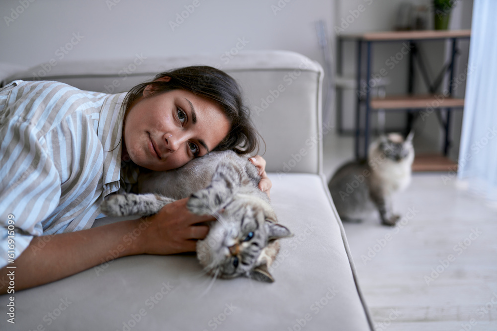 Smiling woman lying with cat on sofa in living room at home Smiling woman lying with cat on sofa in living room at home