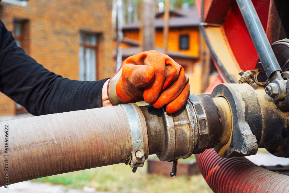 a hand connects a suction hose to a sewage tanker truck. Sewer pumping