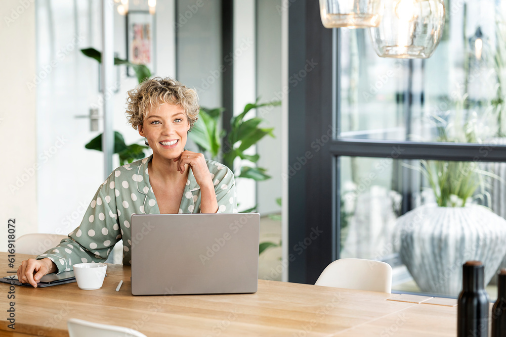 Smiling businesswoman sitting with laptop at table Smiling businesswoman sitting with laptop at table
