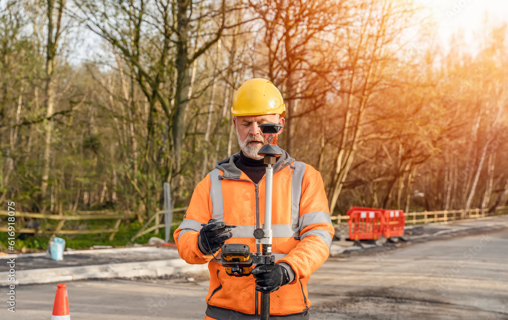 Site engineer operating his touch screen controller instrument during roadworks. Builder using