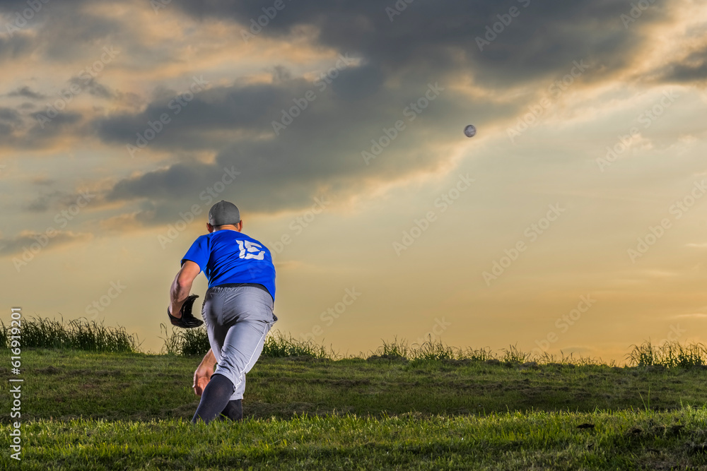 Man throwing baseball standing in grass at dusk Man throwing baseball standing in grass at dusk