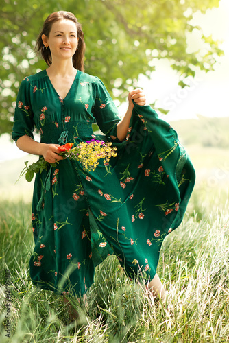 a young girl in a green dress,with a bouquet of flowers,stands in the wind in a field,the wind blows her dress,it develops in the air,the atmosphere of freedom, flight, vacation,a state of lightness