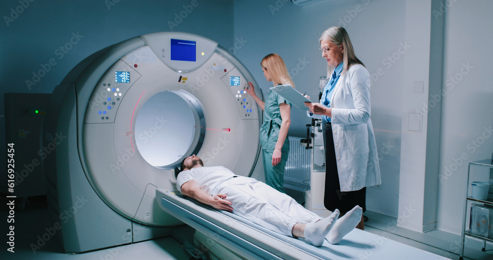 Young man lies down in MRI capsule. Chief head doctor in dressing gown