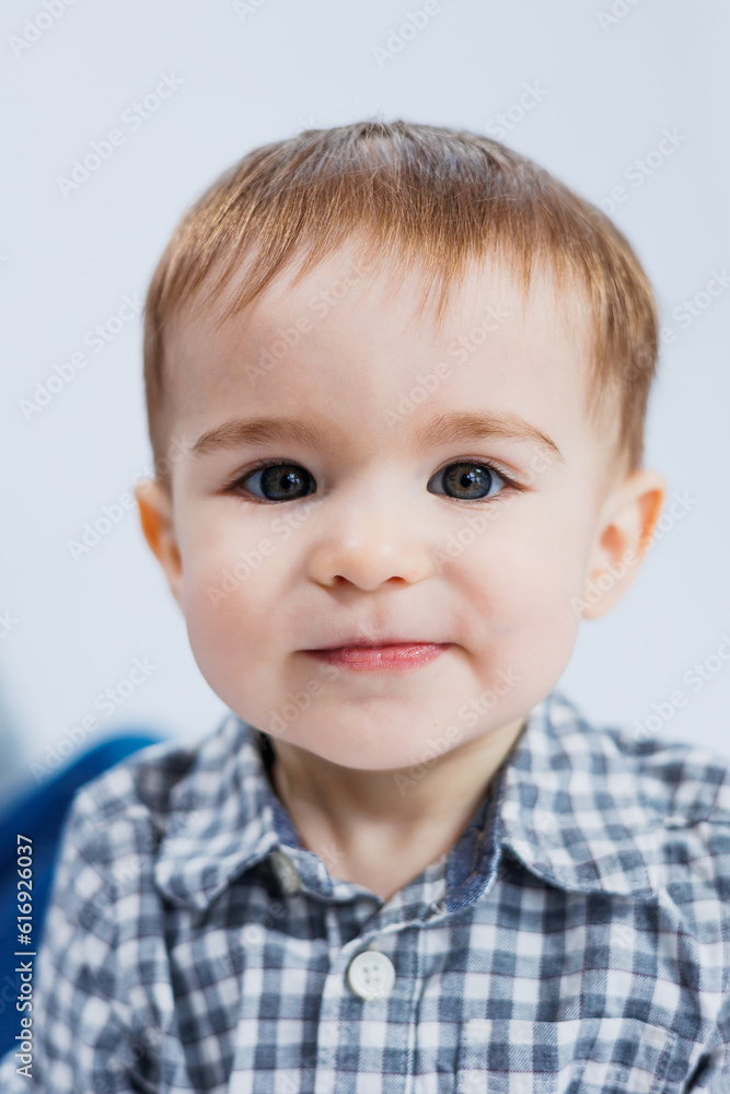 A little boy one year old on a white background in a checkered shirt. A small child with a smile on his face. A little boy one year old on a white background in a checkered shirt. A small child with a smile on his face.