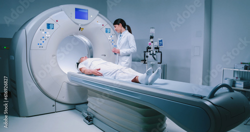 Female medical worker dressed up in gown before MRI examination. Female doctor is preparing patient for magnetic resonance procedure. Patient is lying at CT scanner bad and waiting to be scanned. photo