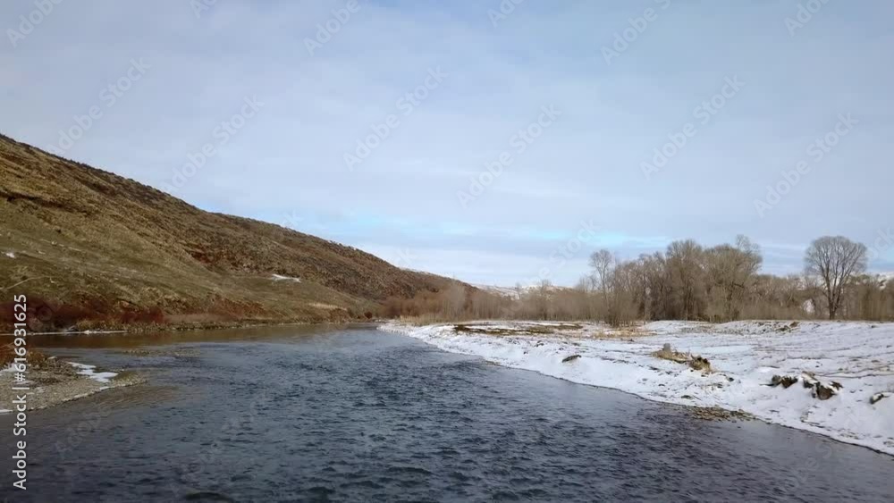 Aerial: Drone Panning Forward Over River Amidst Bare Trees On Snow Near Mountains Against Sky - Billings, Montana Aerial: Drone Panning Forward Over River Amidst Bare Trees On Snow Near Mountains Against Sky - Billings, Montana