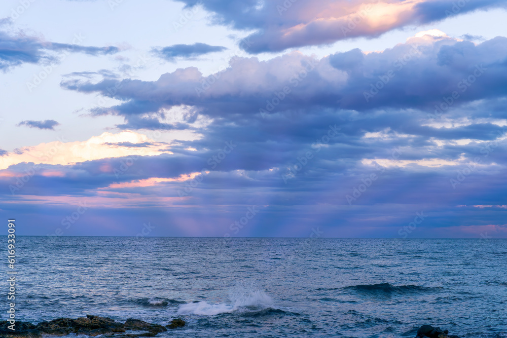 Obraz premium amazing evening or morning sea shore landscape of blue water, rock coast and unique natural phenomenon of glow from below the sea to amazing sunset colorful clouds