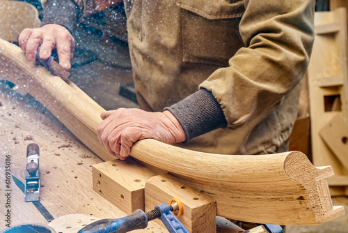 Fototapeta Carpenter sands bending wooden railing with sandpaper in workshop closeup