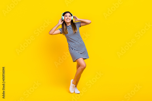 Full body photo of young chinese lady touch wireless headphones rest listen itunes music have fun isolated on yellow color background © deagreez