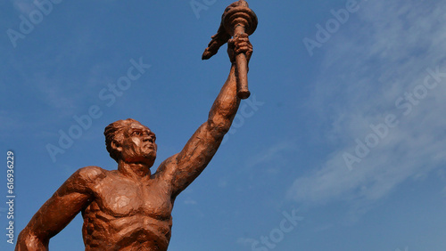 Surakarta, Indonesia, 20th June 2023, Statue of spirit of sport in a form of man holding torch against blue sky, Patung obor manahan located at the Manahan stadium Surakarta photo