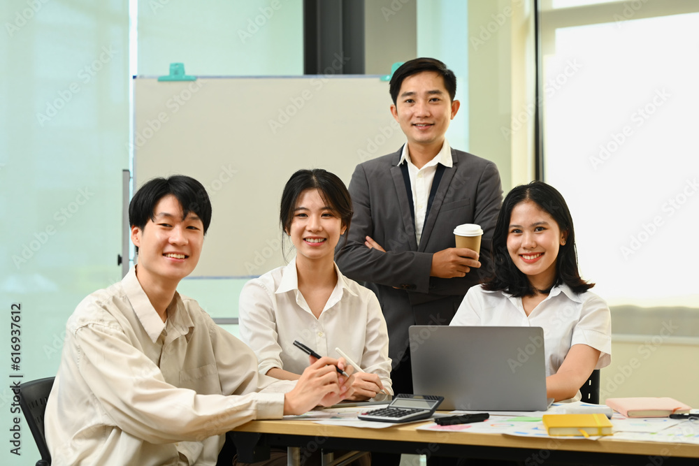 Group of company employees sitting in modern office and smiling confidently to camera