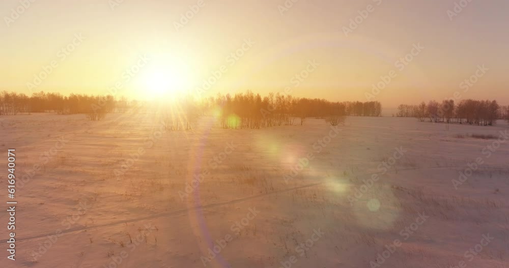 Aerial drone view of cold winter landscape with arctic field, trees covered with frost snow and morning sun rays over horizon. Extreme weather. Aerial drone view of cold winter landscape with arctic field, trees covered with frost snow and morning sun rays over horizon. Extreme weather.