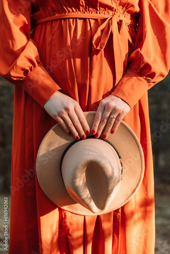 Junge Frau in oranger Kleid hält in den Händen ein Hut in Country-Stil
