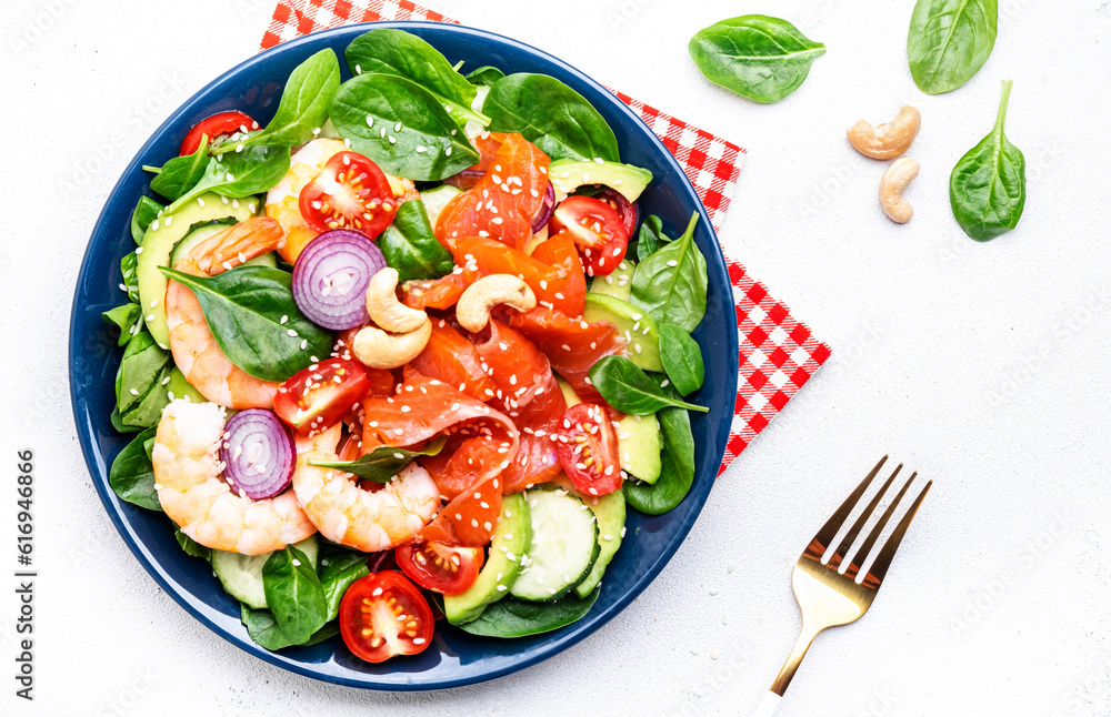 Fresh salad for keto diet with shrimp, salmon, avocado, spinach, cucumber, tomato, cashew nuts, sesame. Low-carbohydrate lunch rich in healthy fats. White table background, top view