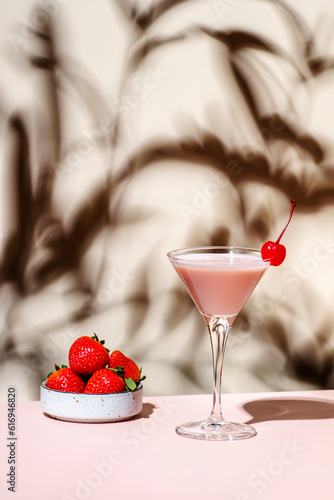 Bounty martini summer cocktail drink with vodka, liqueur, cream, strawberries and ice in glass with red cocktail cherry. Beige pink background