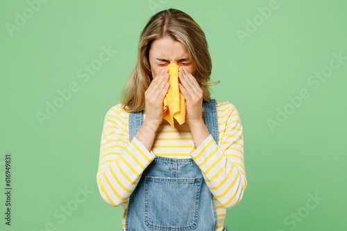 Sick unhealthy ill allergic woman has red watery eyes runny stuffy sore nose suffer from allergy trigger symptom hay fever cover mouth sneeze isolated on plain pastel green background studio portrait photo