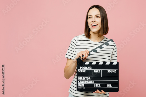 Young smiling happy fun woman she wearing casual clothes t-shirt hold in hand classic black film making clapperboard isolated on plain pastel light pink background studio portrait. Lifestyle concept.