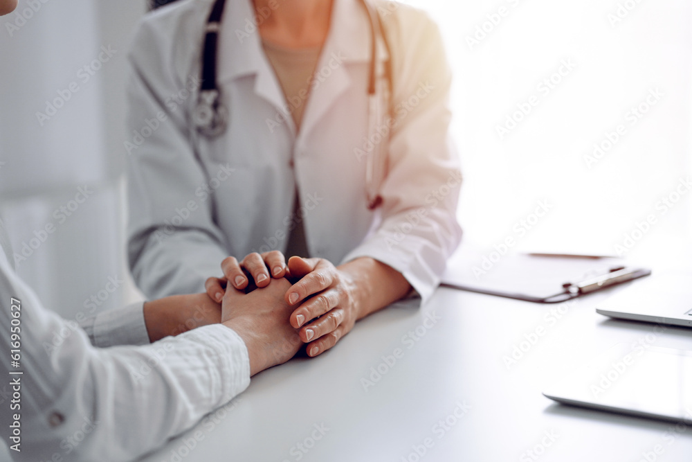 Doctor and patient sitting at the desk in clinic office. The focus is on female physician's hands reassuring woman, close up. Perfect medical service, empathy, and medicine concept