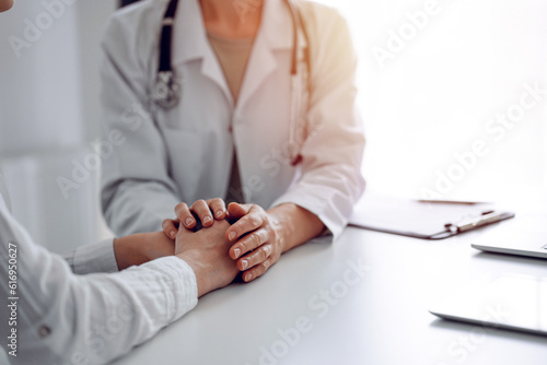 Doctor and patient sitting at the desk in clinic office. The focus is on female physician's hands reassuring woman, close up. Perfect medical service, empathy, and medicine concept