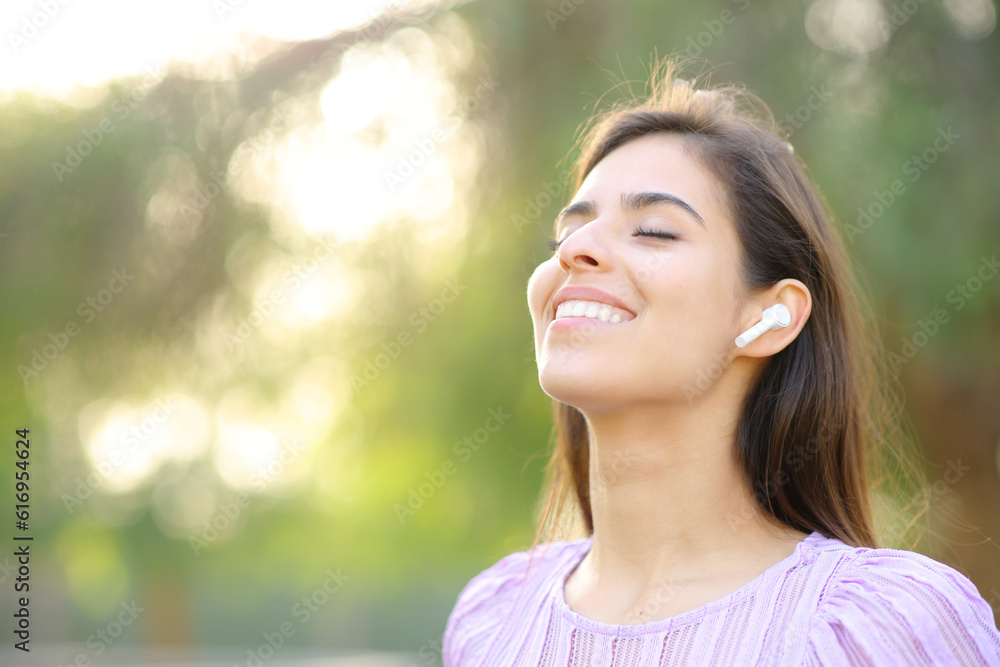 Happy woman breathing fresh air wearing earbud Happy woman breathing fresh air wearing earbud