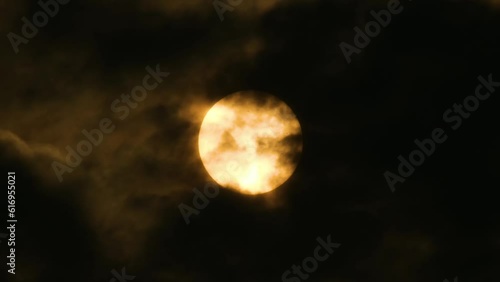 Radiant orange moon in night sky as dark clouds move. Static close-up shot photo