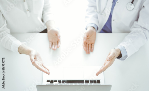 Doctor and patient sitting near each other at the table in clinic. The focus is on female hands pointing into tablet computer touchpad together. Medicine concept photo