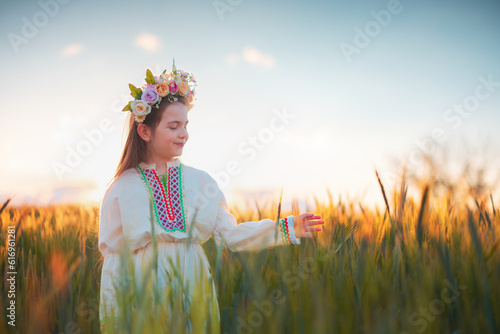 Beautiful young girl with flower chaplet, ethnic folklore dress with traditional Bulgarian embroidery during sunset on a wheat agricultural field photo
