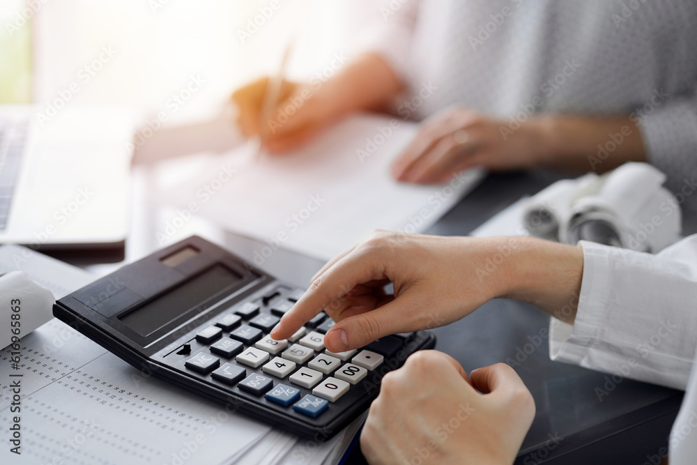 Woman accountant using a calculator and laptop computer while counting taxes for a client. Business audit and finance concepts Woman accountant using a calculator and laptop computer while counting taxes for a client. Business audit and finance concepts