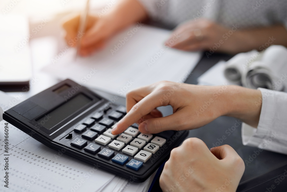 Woman accountant using a calculator and laptop computer while counting taxes for a client. Business audit and finance concepts Woman accountant using a calculator and laptop computer while counting taxes for a client. Business audit and finance concepts