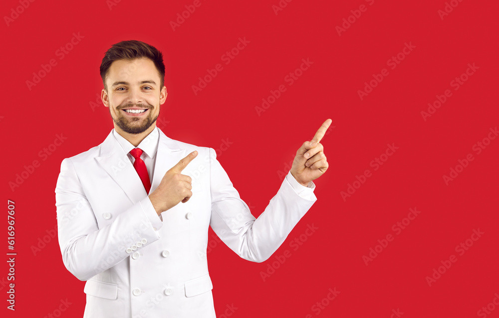 Portrait of smiling young Caucasian man in suit isolated on red studio background point at blank copy space aside. Happy handsome male in costume recommend sale deal or promotion offer. Portrait of smiling young Caucasian man in suit isolated on red studio background point at blank copy space aside. Happy handsome male in costume recommend sale deal or promotion offer.