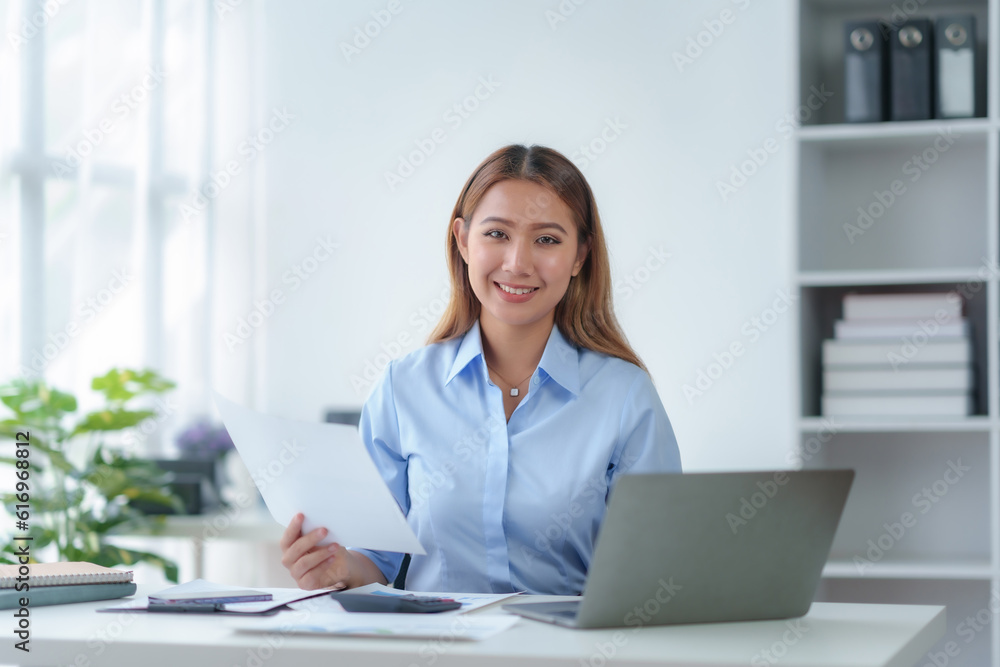 Beautiful young business woman manager or company worker holding accounting document, checking financial data or marketing report working in office with laptop. Accountant consults on some docum Beautiful young business woman manager or company worker holding accounting document, checking financial data or marketing report working in office with laptop. Accountant consults on some docum