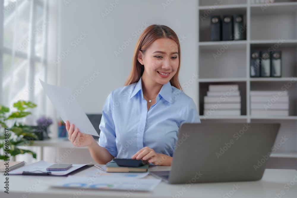 Beautiful young business woman manager or company worker holding accounting document, checking financial data or marketing report working in office with laptop. Accountant consults on some docum Beautiful young business woman manager or company worker holding accounting document, checking financial data or marketing report working in office with laptop. Accountant consults on some docum
