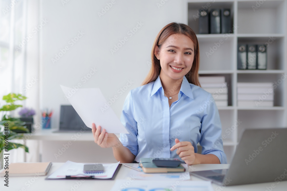 Beautiful young business woman manager or company worker holding accounting document, checking financial data or marketing report working in office with laptop. Accountant consults on some docum Beautiful young business woman manager or company worker holding accounting document, checking financial data or marketing report working in office with laptop. Accountant consults on some docum