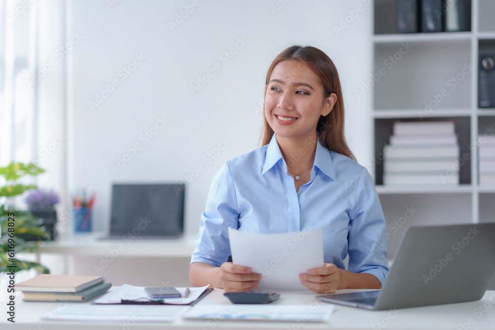 Beautiful young business woman manager or company worker holding accounting document, checking financial data or marketing report working in office with laptop. Accountant consults on some docum Beautiful young business woman manager or company worker holding accounting document, checking financial data or marketing report working in office with laptop. Accountant consults on some docum