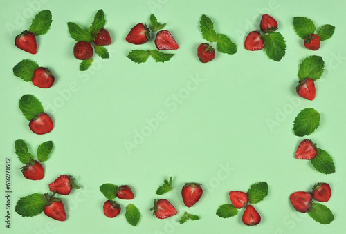 Frame made of fresh ripe strawberries and green mint leaves on light green background. Top view, flat lay. Free copy space