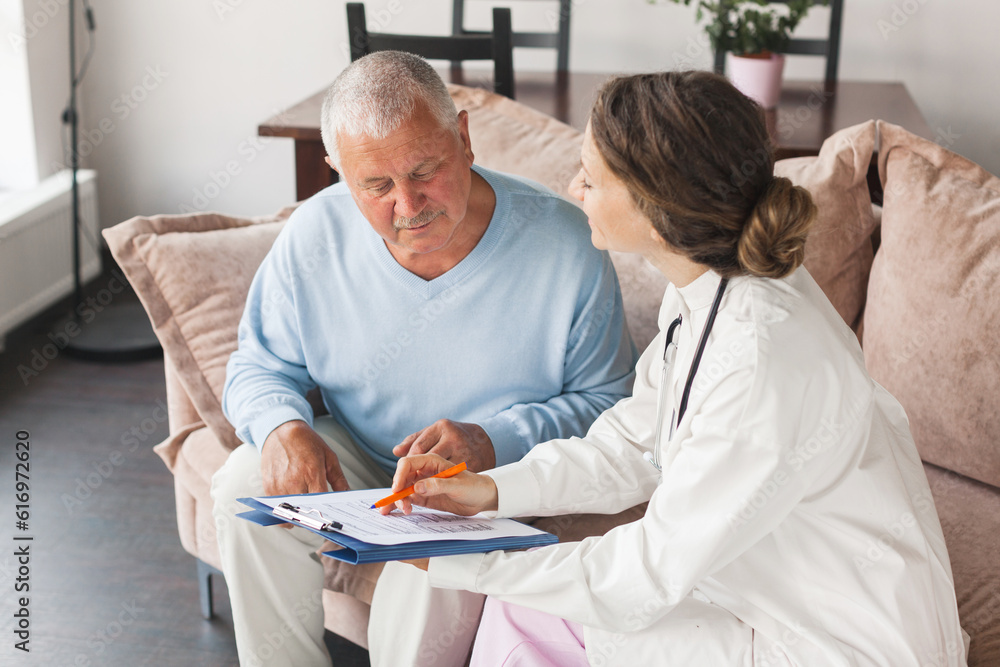 Female professional doctor showing medical test result explaining prescription using clipboard visiting senior elderly old man patient at home sitting on sofa Female professional doctor showing medical test result explaining prescription using clipboard visiting senior elderly old man patient at home sitting on sofa
