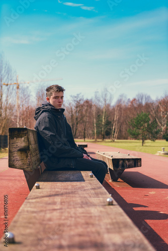 portrait of a teenager in an anorak sitting on a park bench