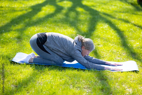 Mature woman in grey sportswera doing yoga in the park