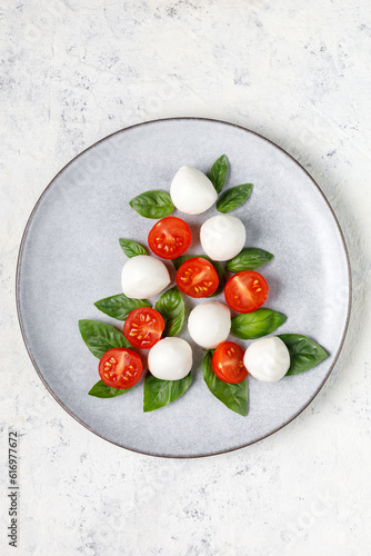 Caprese salad in the form of a Christmas tree. Festive tomato mozzarella and basil appetizer on light plate.