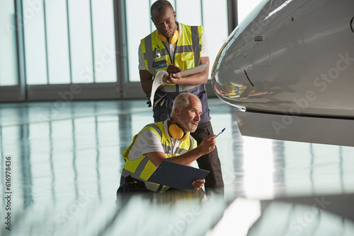 Airport ground crew workers examining airplane in hangar