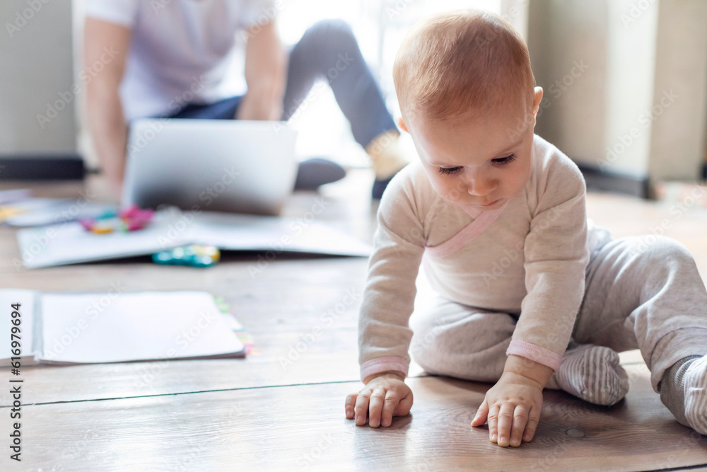 Baby daughter sitting on floor near father working at laptop