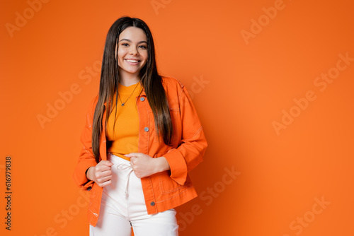 Foto Fashionable and brunette teenage girl in denim jacket and pants smiling while lo
