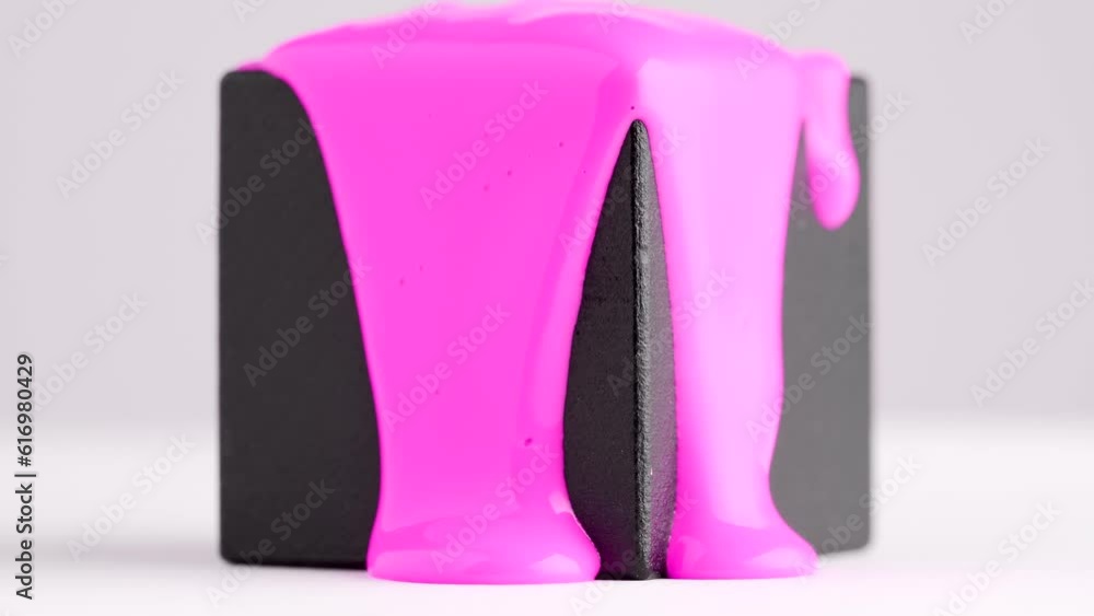 Bright pink paint runs down the black cube. Creative concept. Pink liquid drops of paint flow down the cube on white. Viscous pink liquid flowing down the surface of black cube in streams. Bright pink paint runs down the black cube. Creative concept. Pink liquid drops of paint flow down the cube on white. Viscous pink liquid flowing down the surface of black cube in streams.