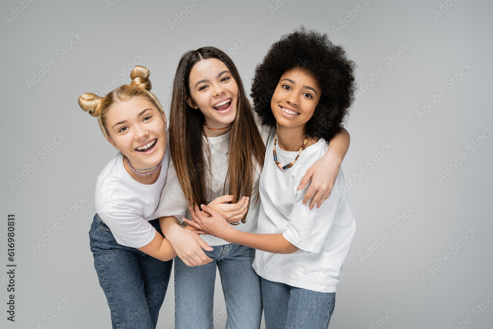 Positive multiethnic teen girls in white t-shirts and jeans hugging