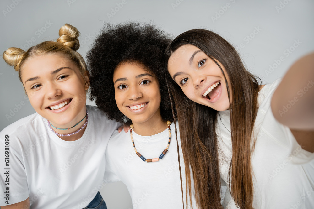 Excited and cheerful teenage girls in white t-shirts looking at camera and hugging each other while spending time together isolated on grey, teenage friends having fun together Excited and cheerful teenage girls in white t-shirts looking at camera and hugging each other while spending time together isolated on grey, teenage friends having fun together