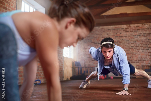 Young man with headphones doing one-arm push-ups in gym studio