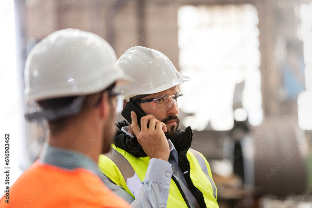 Steel workers talking on cell phone in factory Steel workers talking on cell phone in factory