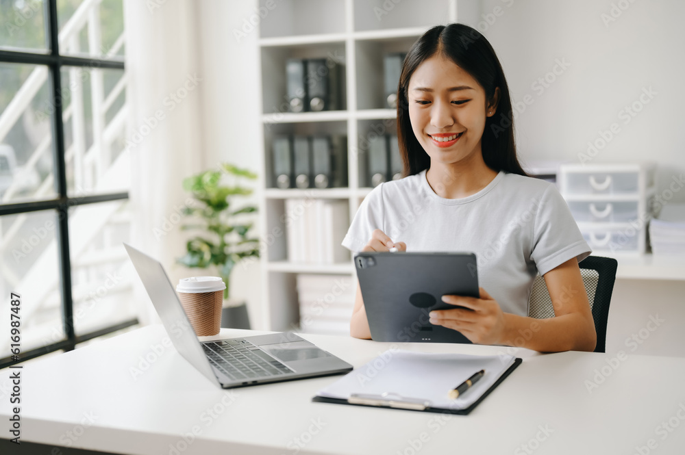 Successful Asian Businesswoman Analyzing Finance on Tablet and Laptop at Office Desk tax, report, accounting, statistics, and analytical research concept. Successful Asian Businesswoman Analyzing Finance on Tablet and Laptop at Office Desk tax, report, accounting, statistics, and analytical research concept.