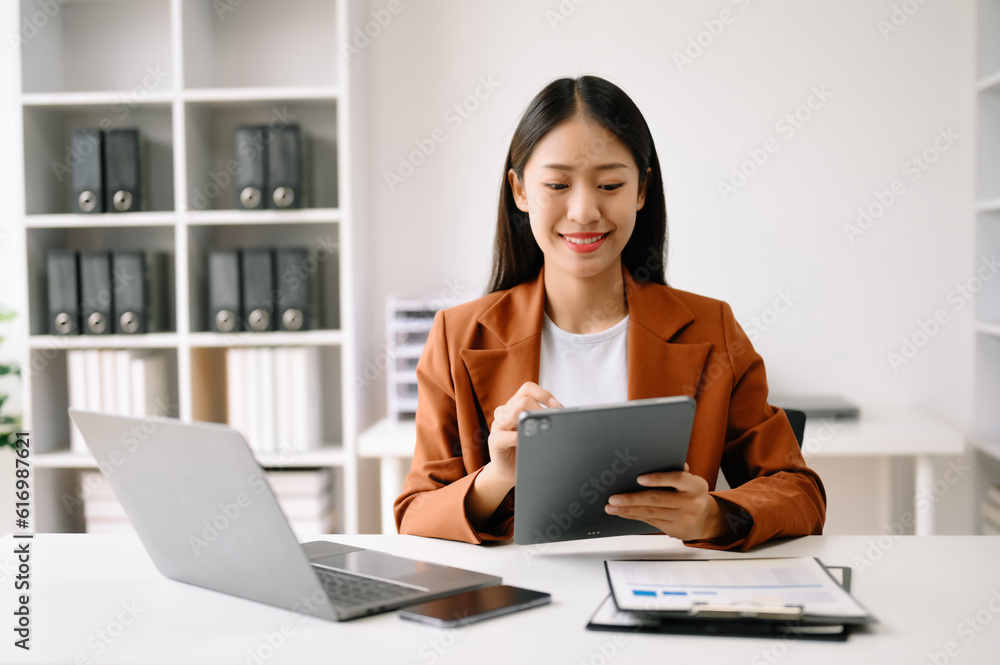 Successful Asian Businesswoman Analyzing Finance on Tablet and Laptop at Office Desk tax, report, accounting, statistics, and analytical research concept. Successful Asian Businesswoman Analyzing Finance on Tablet and Laptop at Office Desk tax, report, accounting, statistics, and analytical research concept.
