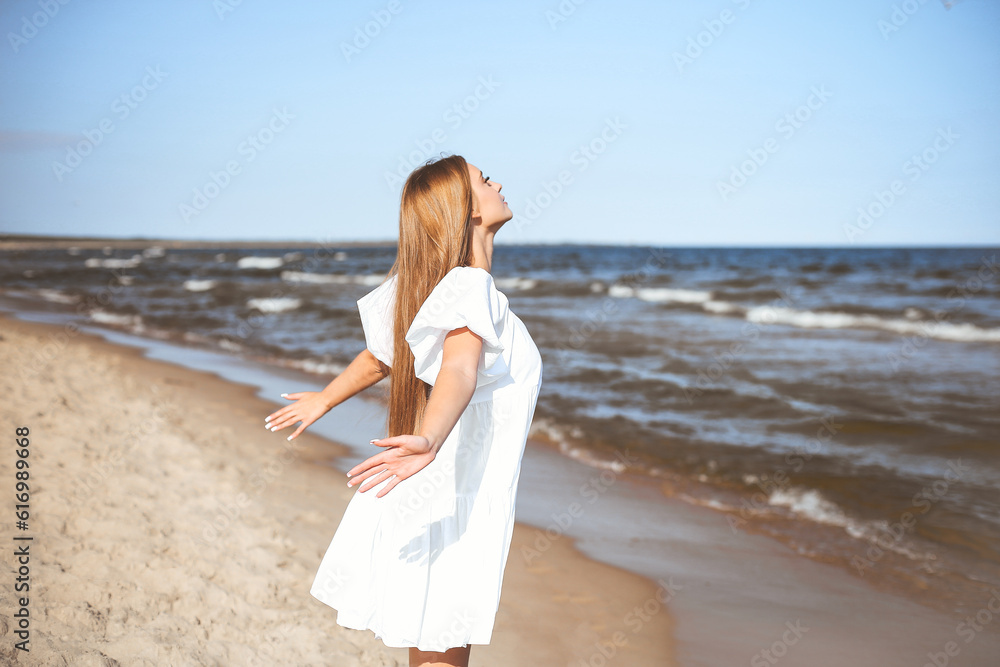 Happy smiling beautiful woman is on the ocean beach in a white summer dress, open arms Happy smiling beautiful woman is on the ocean beach in a white summer dress, open arms